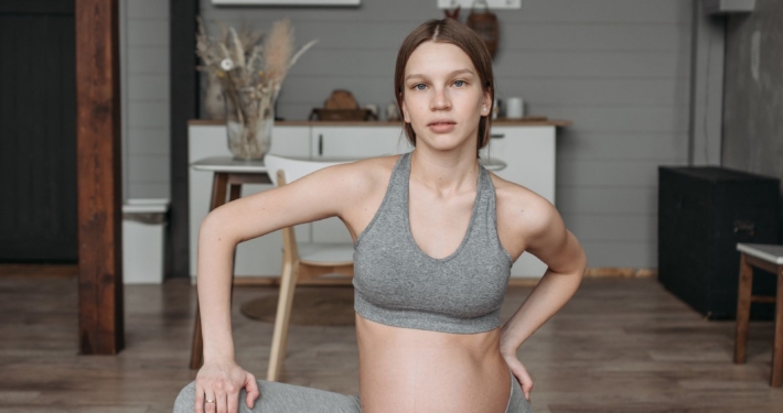 Zwangere vrouw in grijze, comfortabele sportkleding doet thuis een rustige yogaoefening