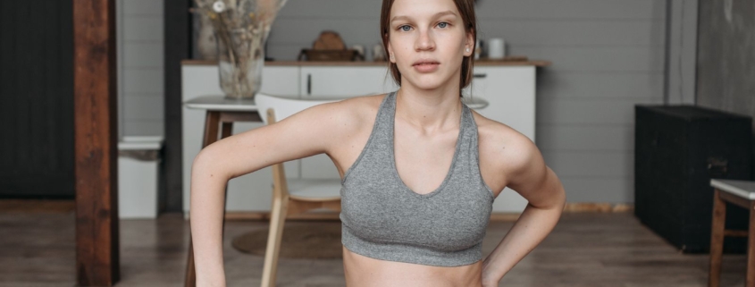 Zwangere vrouw in grijze, comfortabele sportkleding doet thuis een rustige yogaoefening